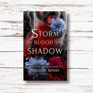 May include: Book cover with a dark background featuring red and blue flowers, lightning bolts, and the title "Storm of Blood and Shadow" with the subtitle "Merciless Dragons Book 3" and the author's name "Rebecca F. Kenney".