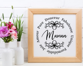 May include: A square wooden frame containing a white print with the word Maman in the center, surrounded by a circular arrangement of the words Amour, Pure, Douceur, Fabuleuse, Unique, Formidable, and Joie, accented by two black floral line art icons.