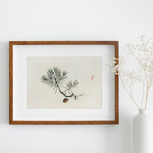 May include: A framed print of a black and white ink drawing of a pine branch with a single pine cone. The print is in a brown wooden frame and is hanging on a white wall. A vase with white flowers is on the right side of the image.
