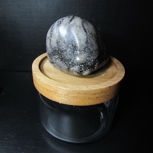 May include: A black and white fossilized stone with a wooden lid on top of a clear glass jar.