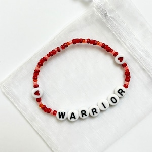 May include: Red and pink beaded bracelet with white beads spelling out the word "WARRIOR" and two red heart beads.