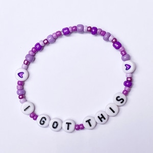 May include: Purple and white beaded bracelet with the words "I GOT THIS" and two small purple hearts.