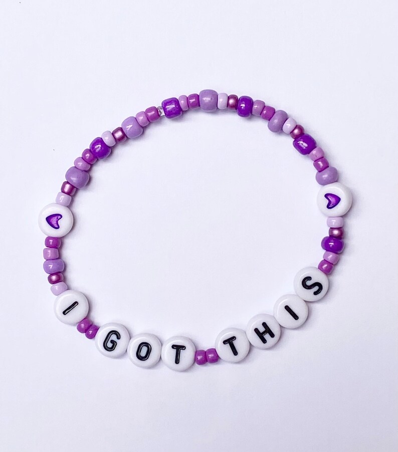 May include: Purple and white beaded bracelet with the words "I GOT THIS" and two small purple hearts.