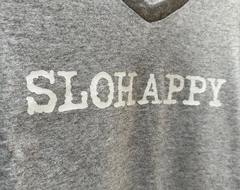 Könnte beinhalten: Graues V-Ausschnitt-T-Shirt mit dem Wort "SLOHAPPY" in weiß auf der Vorderseite.
