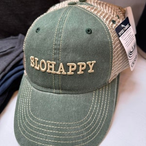 May include: A green and tan baseball cap with a mesh back. The front of the cap has the words "SLOHAPPY" embroidered in gold thread.