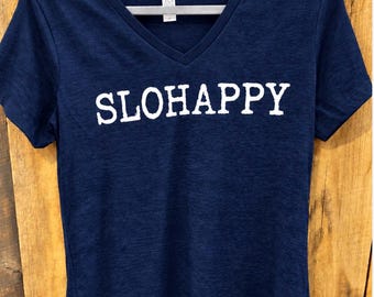 Könnte beinhalten: Ein kurzärmeliges V-Ausschnitt-T-Shirt in Marineblau mit melierter Textur. Auf der Brust ist das Wort SLOHAPPY in weißen Großbuchstaben aufgedruckt. Es hängt an einem grauen Kunststoffkleiderbügel vor einem Hintergrund aus vertikalen Holzbrettern.