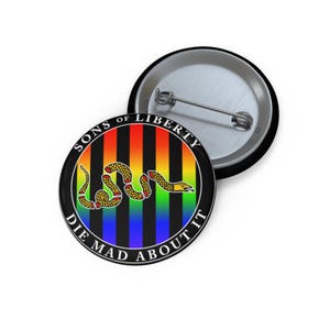 May include: A round button with a black border and a rainbow striped background. The button features a yellow snake coiled in the center, with the text "SONS OF LIBERTY" and "DIE MAD ABOUT IT" in a circular pattern.