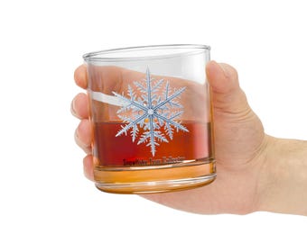 May include: A clear glass tumbler with a snowflake design and the text "Snowflake Tear Collector". The glass is filled with a dark amber liquid.