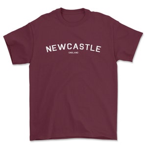 May include: Burgundy t-shirt with white text that reads "NEWCASTLE ENGLAND"
