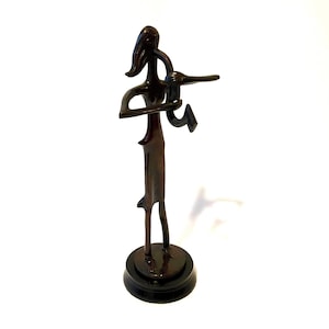 Puede incluir: Una escultura de bronce de una persona tocando un instrumento musical. La figura tiene una forma esbelta con extremidades alargadas y está montada sobre una base redonda y negra. El color marrón oscuro y el diseño abstracto de la escultura le dan una estética moderna.