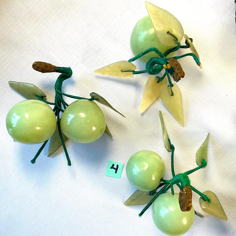 K&ouml;nnte beinhalten: Drei dekorative Jade-Fruchtarrangements. Jedes Arrangement zeigt hellgr&uuml;ne, runde Fr&uuml;chte mit hellgelben Bl&auml;ttern und gr&uuml;nen Stielen. Ein Arrangement hat die gr&uuml;ne Zahl 4 auf wei&szlig;em Hintergrund.