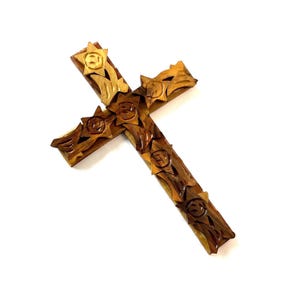 May include: A wooden cross with intricate carvings of flowers and leaves. The cross is made of a light brown wood with darker brown accents.