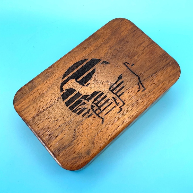 May include: A rectangular wooden box with rounded edges. The box is made of a dark brown wood and features a black graphic design on the top. The design appears to be a stylized image of a horse and a globe.