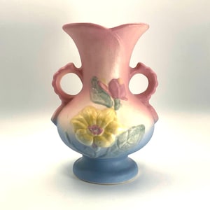 May include: A vintage ceramic vase in pastel colors. The vase features a pink top, a light yellow and blue body, and a blue base. It has two loop handles and is decorated with a yellow flower and pink buds.