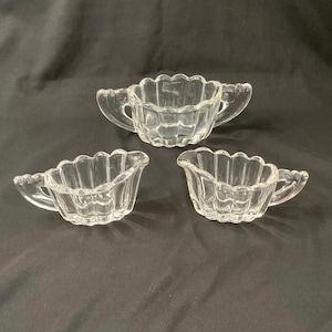 May include: Three clear glass serving dishes with fluted sides and handles. The dishes are arranged in a triangular pattern on a black surface.