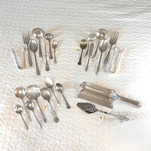 May include: A collection of silver-toned metal flatware and serving utensils arranged in four groups labeled 1 through 4. The set includes various spoons, forks, tongs, a butter knife, a decorative server, and a rectangular tray with a handle.