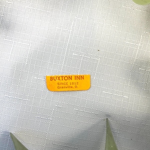 K&ouml;nnte beinhalten: Ein orangefarbener Buxton Inn-Aufkleber mit dem Text "BUXTON INN SINCE 1812 Granville, O." wird vor einem hellgrauen, strukturierten Hintergrund angezeigt. Der Aufkleber ist rechteckig mit abgerundeten Ecken.