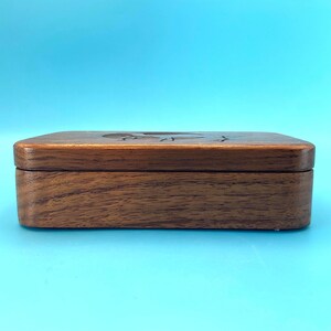 May include: A rectangular wooden box with a dark brown finish. The box has a lid with a carved design on top. The box is sitting on a light blue surface.
