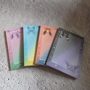 May include: Four colorful notepads with gradient backgrounds and character illustrations. Each notepad features a different color scheme: pink, blue, orange, and purple. The notepads have lined pages and star accents.