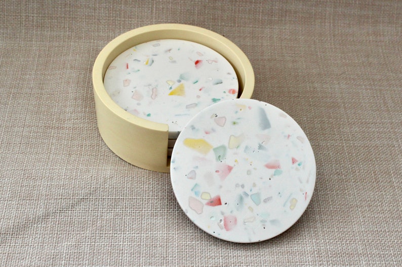 May include: Set of six round coasters with a white base and colorful flecks. The coasters are in a cream-colored holder.