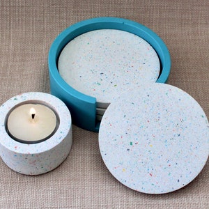 May include: Set of six white speckled coasters with colorful flecks, in a blue holder. A matching white speckled candle holder with a lit candle is also shown.