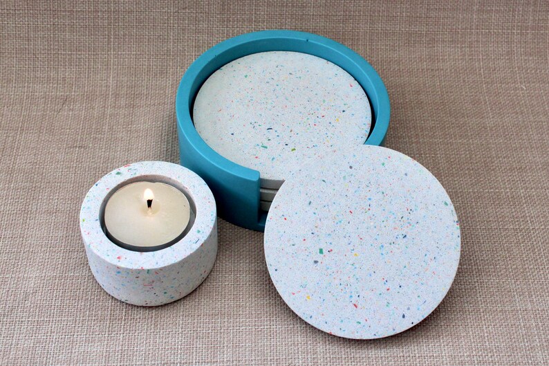 May include: Set of six white speckled coasters with colorful flecks, in a blue holder. A matching white speckled candle holder with a lit candle is also shown.