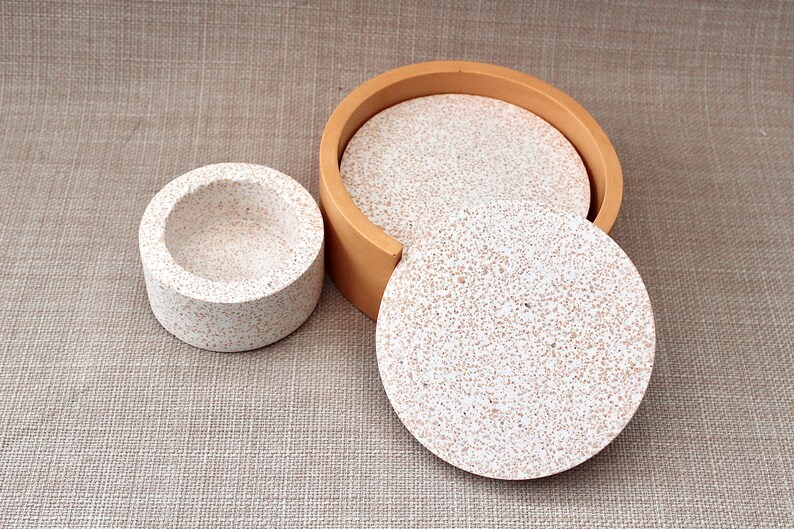 May include: Set of four round coasters with a speckled white and brown design. The coasters are stacked and have a wooden frame.