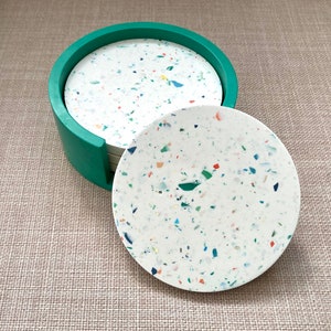May include: Set of six round coasters with a white base and colorful flecks. The coasters are in a green holder.