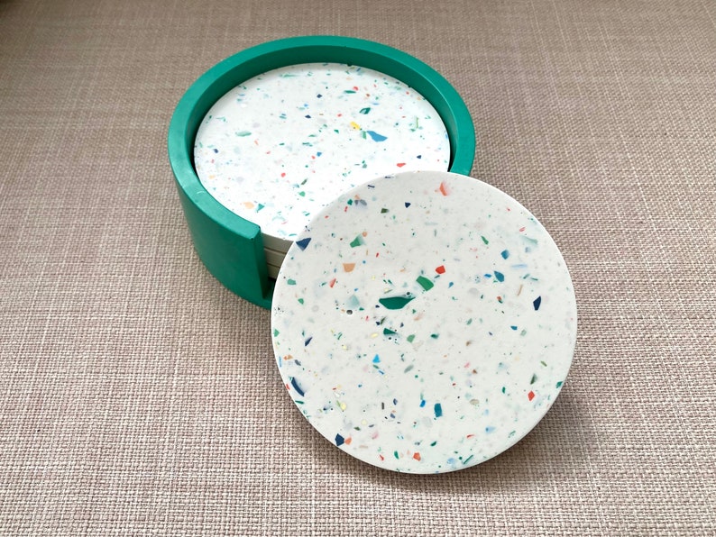 May include: Set of six round coasters with a white base and colorful flecks. The coasters are in a green holder.