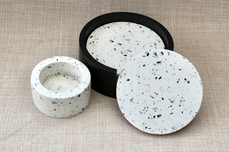 May include: Three round coasters made of white speckled resin with black flecks. The largest coaster has a black rim.