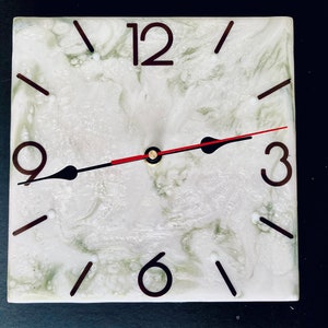 May include: A white clock face with black numbers and hands. The clock face has a marbled design with green and white swirls. The clock is set to 3:00.