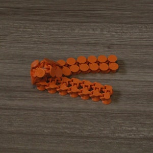 Puede incluir: Primer plano de una cadena de conectores de plástico naranja. Los conectores están unidos en un patrón en zigzag.