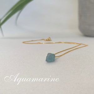 Peut inclure: Un collier délicat en chaîne dorée avec un pendentif en pierre d'aquamarine bleu clair. La pierre précieuse est un cristal brut et naturel avec une forme irrégulière et rugueuse. Le collier est simple et élégant, parfait pour tous les jours.