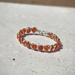 Könnte beinhalten: Ein Ring aus silbernem Draht mit orangefarbenen Karneolperlen.