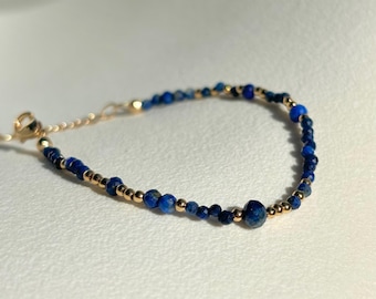 May include: A delicate gold bracelet with small blue lapis lazuli beads. The bracelet has a simple clasp closure.