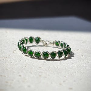 May include: A silver wire ring with green gemstone beads. The wire is twisted and the beads are evenly spaced.