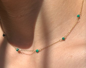 May include: A gold chain necklace with small green gemstone beads. The necklace is worn on a person's neck.