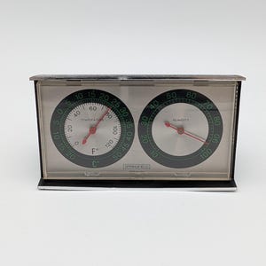 May include: A rectangular Springfield brand weather station featuring two circular analogue gauges. The left gauge displays temperature in Fahrenheit and Celsius, while the right gauge measures humidity. Both dials have red needles and black text.