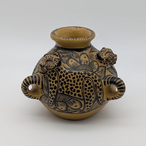 Peut inclure: Un vase en céramique beige avec des motifs léopard noirs et deux anses. Le vase présente deux sculptures de têtes de léopard et un bord noir. Le corps du vase est décoré de motifs floraux noirs.