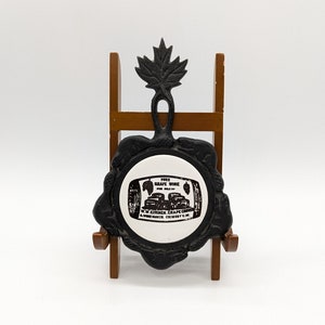 May include: Black cast iron bottle stopper with a maple leaf design. The stopper features a white label with the text "Pure Grape Wine For Sale By W.W. Kitchen, Grape Co. A Winemaker Grimsby, Ont."