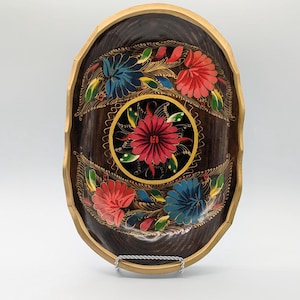 May include: An oval wooden tray with a dark brown background and a gold rim. The tray is decorated with hand-painted flowers in shades of red, blue, and green.