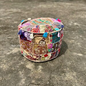 Può includere: Pouf rotondo patchwork con un vivace mix di colori e motivi. La parte superiore presenta un disegno centrale circondato da vari quadrati di tessuto. I lati sono adornati da nappe colorate. Il testo "RuhiCollection" è visibile.