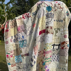 May include: A patchwork quilt with a cream-colored background and a variety of colorful fabric patches. The quilt is hanging outdoors, showcasing its intricate stitching and diverse patterns. The patches include floral, geometric, and abstract designs.