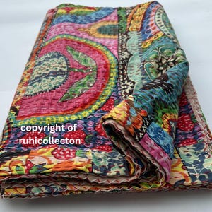 May include: A folded, colorful quilt with a patchwork design. The quilt features a vibrant mix of pink, blue, green, and orange hues. The text "copyright of ruhicollecton" is visible on the quilt.