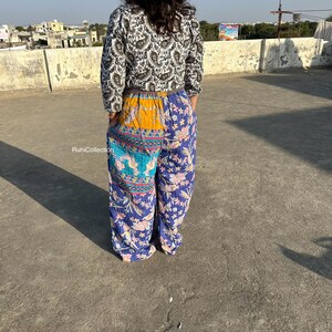 May include: A woman wearing a black and white patterned top with a long sleeve and a pair of blue, yellow, and turquoise patterned pants. The pants have a patchwork design and are wide-legged.