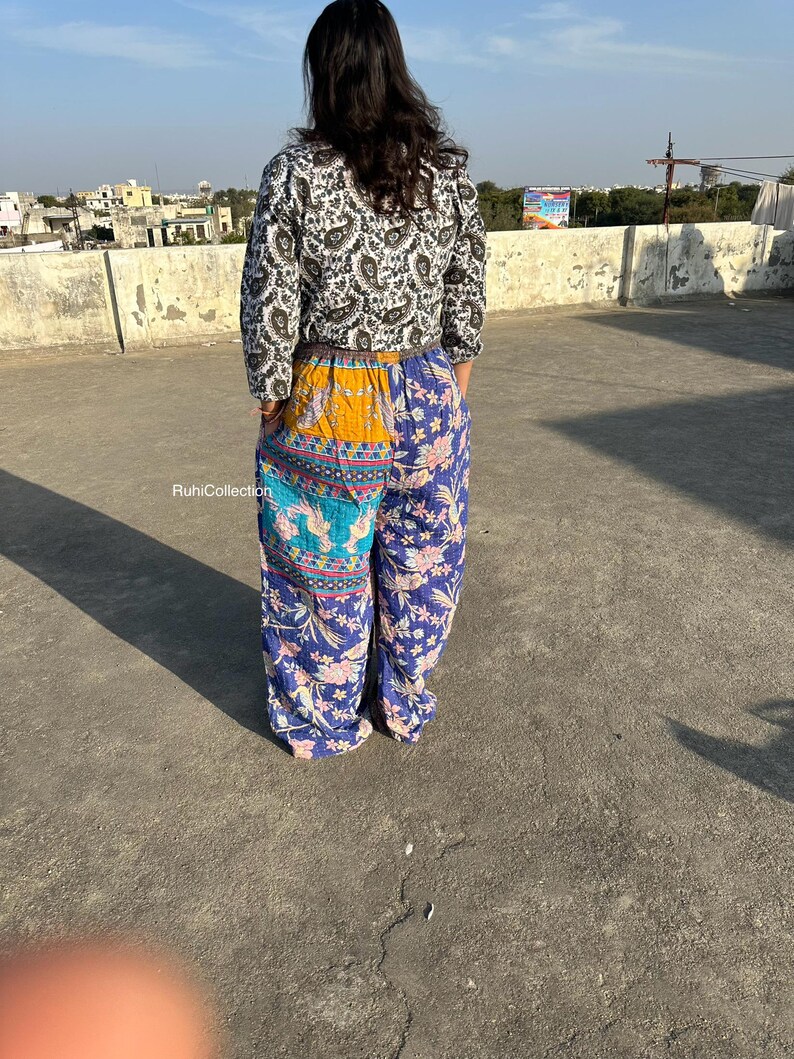 May include: A woman wearing a black and white patterned top with a long sleeve and a pair of blue, yellow, and turquoise patterned pants. The pants have a patchwork design and are wide-legged.