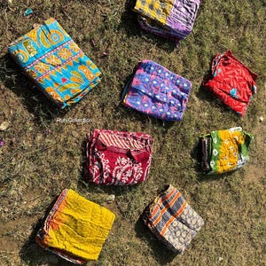 May include: A collection of eight colorful fabric squares with various patterns, including floral, geometric, and paisley designs. The fabric squares are arranged on a bed of green grass.