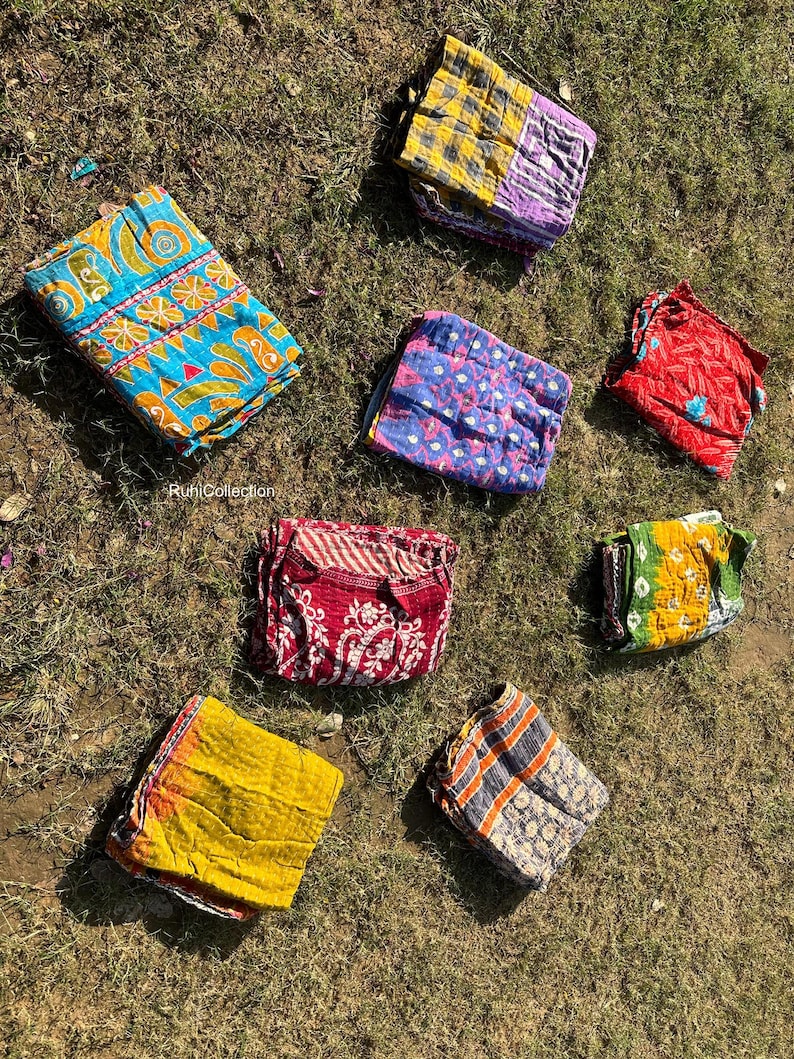 May include: A collection of eight colorful fabric squares with various patterns, including floral, geometric, and paisley designs. The fabric squares are arranged on a bed of green grass.
