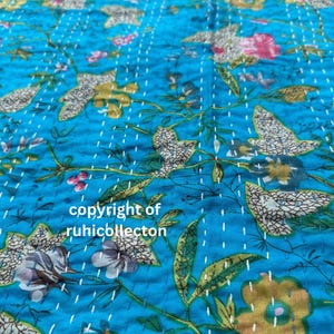 K&ouml;nnte beinhalten: Eine t&uuml;rkisblaue Kantha-Steppdecke mit einem Blumenmuster. Die Steppdecke ist handgen&auml;ht mit wei&szlig;em Garn und zeigt eine Vielzahl von Blumen in den Farben Rosa, Gelb und Gr&uuml;n. Der Text "copyright of ruhicollection" ist in der unteren Mitte des Bildes sichtbar.