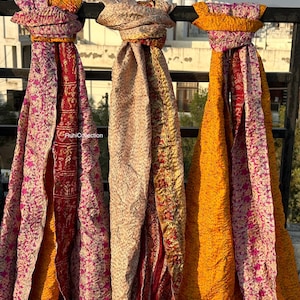 May include: Three colorful silk scarves with a patchwork design. The scarves are hanging on a railing and are made of a variety of fabrics. The scarves are in shades of pink, yellow, and orange.